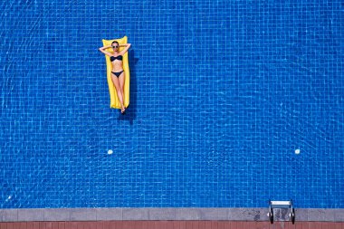 İnce genç kadın bikini üst görünümden sarı şişme büyük yüzme havuzunda.