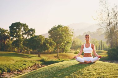 Lotus poz yeşil çimenlerin üzerinde oturan genç kadın