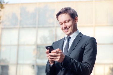 Cep telefonu tutarak ve açık havada duran süre gülümseyen formal giyim neşeli genç adam