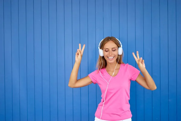 彩色肖像的快乐年轻女子与白色耳机跳舞反对蓝墙 — 图库照片