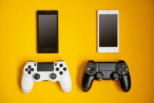 Computer game competition. Gaming concept. White and black smartphones and joysticks on yellow background.