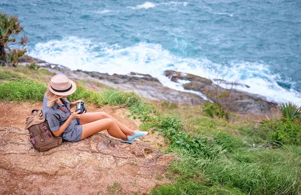 海の景色を楽しんでいるカメラを持ってリュックと帽子の若い女性 — ストック写真