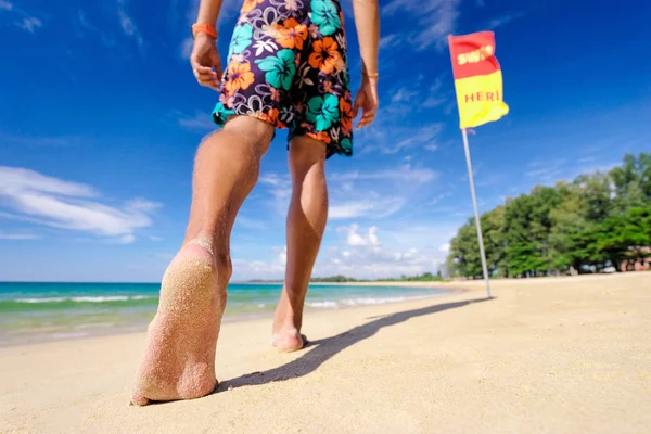 Barefoot man walking on beach at sunny day