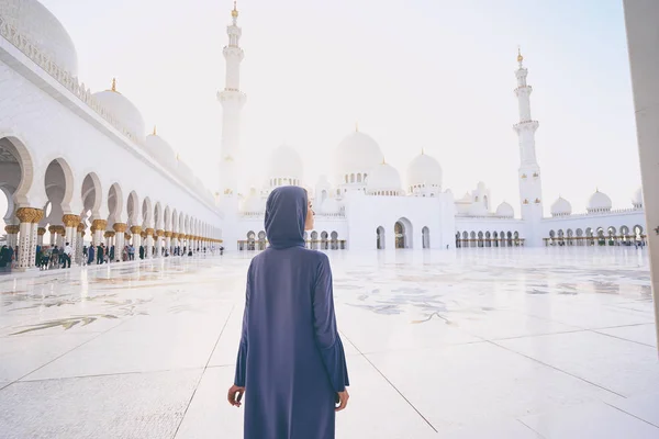 Woman in traditional abaya standing in the Sheikh Zayed Grand Mosque, famous Abu Dhabi sightseeing.