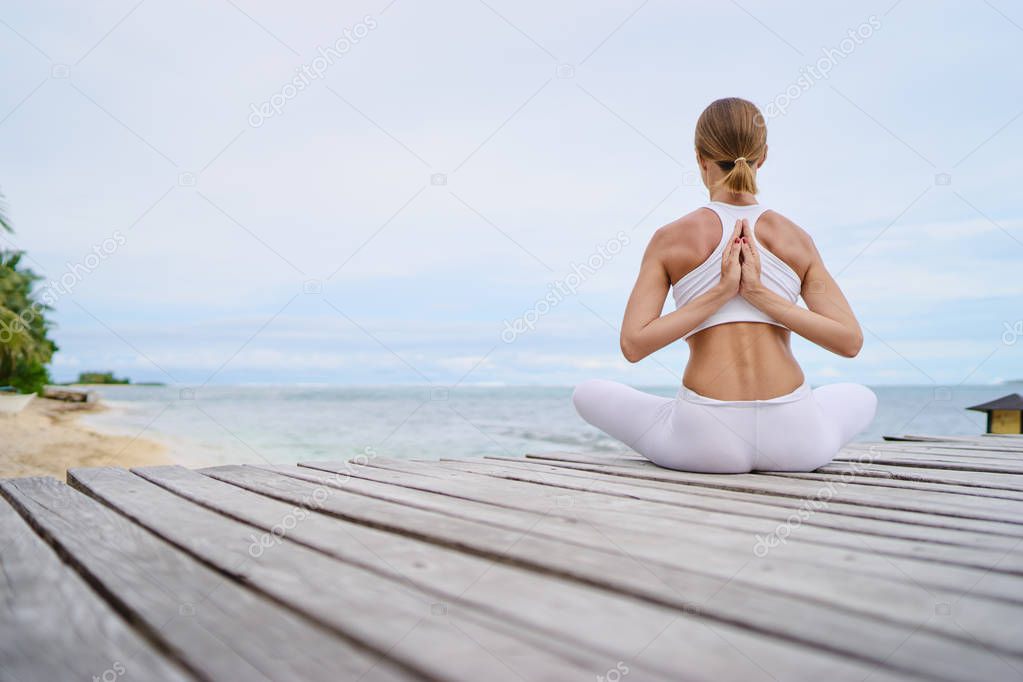 Relaxed young woman in lotus pose on wooden deck with beautiful sea view.