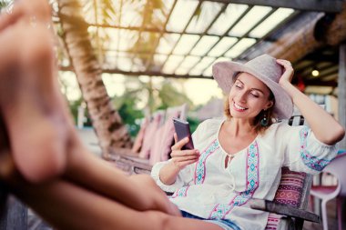 Sahil kafe barda oturan smartphone kullanarak şapkalı genç güzel kadın.