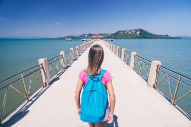 Young woman with rucksack walking on  jetty. clipart