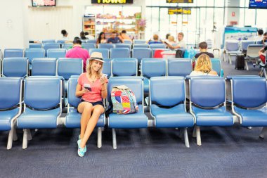 Smartphone kullanarak ve bilet Havaalanı terminal bekleyen uçağa biniş için otururken tutan genç ve güzel kadın.