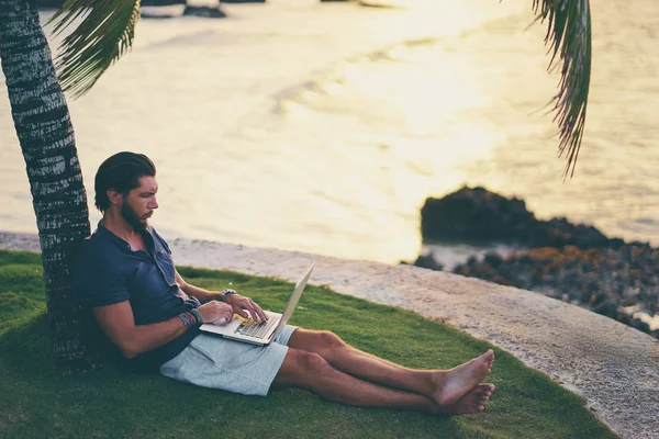 Hombre Joven Que Trabaja Ordenador Portátil Playa Tropical Bajo Palmera —  Fotos de Stock