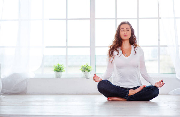 Attractive young woman sitting on lotus position on floor with eyes closed.