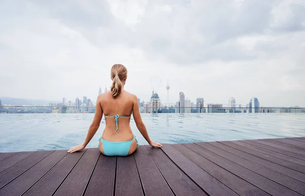 stock image Pretty young woman sittiing near roof top swimming pool with beautiful city view.