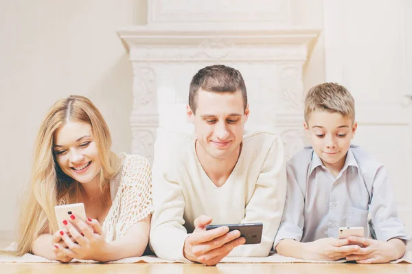 Attractive family couple and son lying on the floor using smart phones.