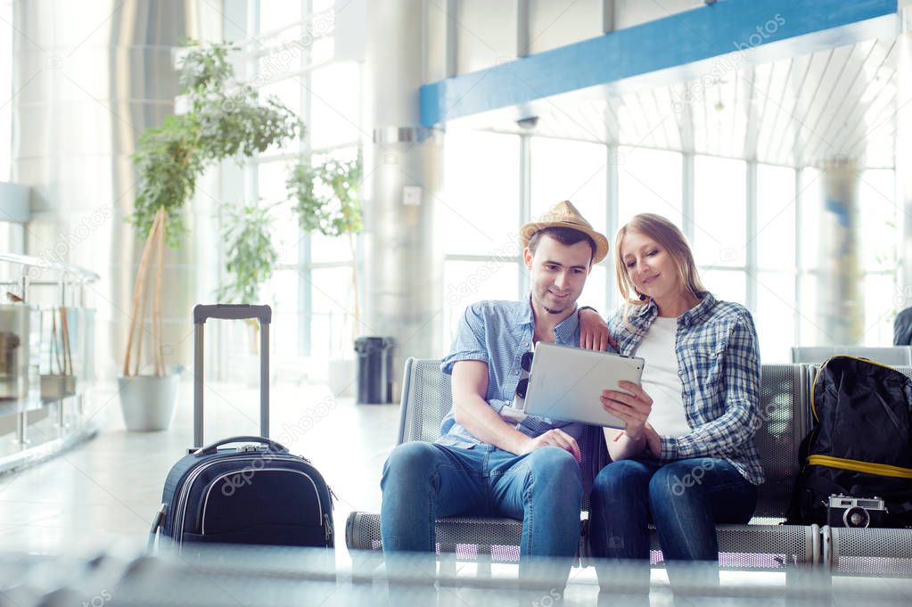 Young loving couple in casual wear using tablet computer while sitting in the airport terminal waiting for boarding.