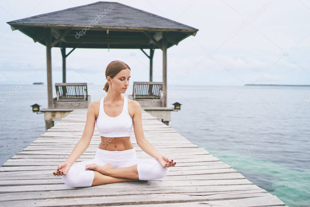 Relaxed young woman in lotus pose on wooden deck with sea view.