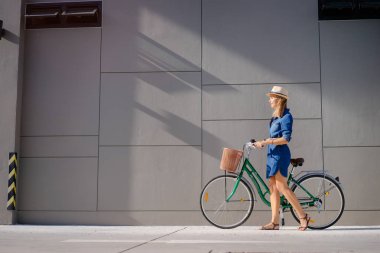 Şapka binicilik bisiklet gri duvara genç ve güzel kadın.