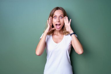 Genç kadın beyaz t-shirt daimi yeşil duvarın karşısında hayrete.