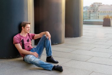 Genç adam casual giyim üzerinde kat açık havada oturma.