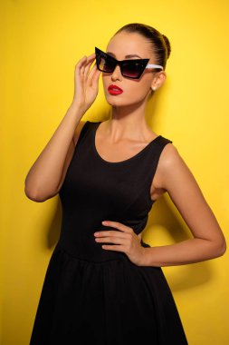Stüdyo portre muhteşem genç kadının küçük siyah elbise sarı arka planı poz.