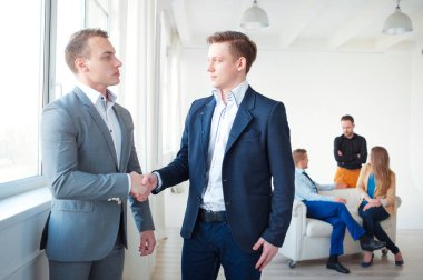 Arka planda konuşurken meslektaşları ile el sıkışan iki emin iş adamları