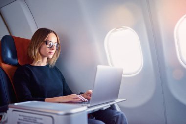 Uçağın içinde otururken dizüstü bilgisayar üzerinde çalışan genç ve güzel iş kadın.