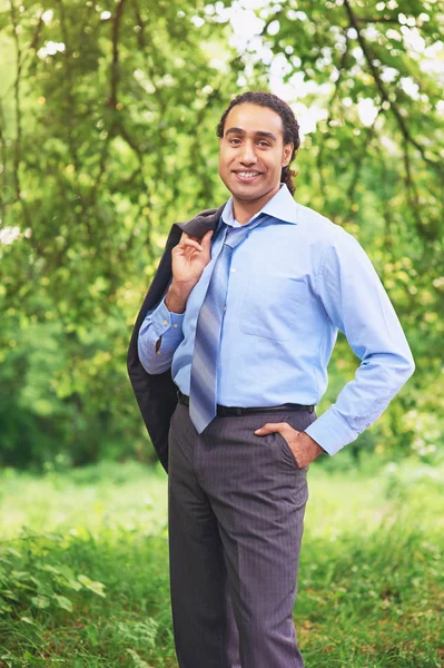 Happy relieved businessman stands in park with his jacket over his shoulder