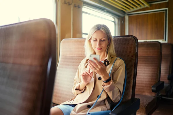 Young pretty woman traveling by the train sitting near the window using smartphone.