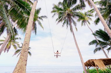 Deniz manzarayı palm grove adlı sallanan beyaz elbiseli mutlu genç kadın.