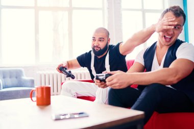 İki yakışıklı genç adam kanepede otururken video oyunları oynarken