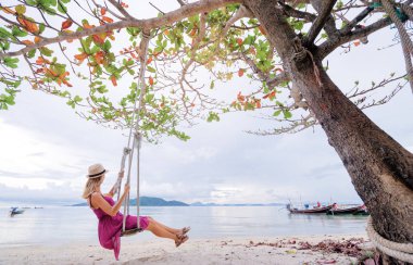 Teeterboard ile Tayland longtail tekneler balıkçılık deniz kenarında üzerinde sallanan mor elbiseli Genç kadın