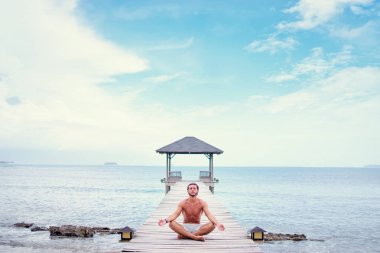 Lotus poz ahşap iskele üzerinde oturan genç adam