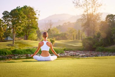 Lotus poz yeşil çimenlerin üzerinde oturan genç kadın. Sakin ve meditasyon kavramı.