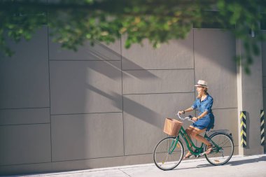 Şapka binicilik bisiklet gri duvara genç ve güzel kadın.