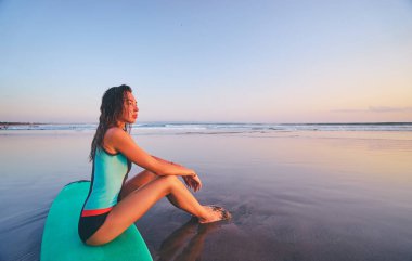 Sörf tahtası Günbatımı keyfi kum üzerine oturan rahat genç kadın.