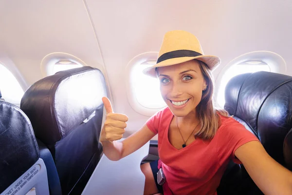 Young woman in plane taking selfie while sitting in airplane seat.