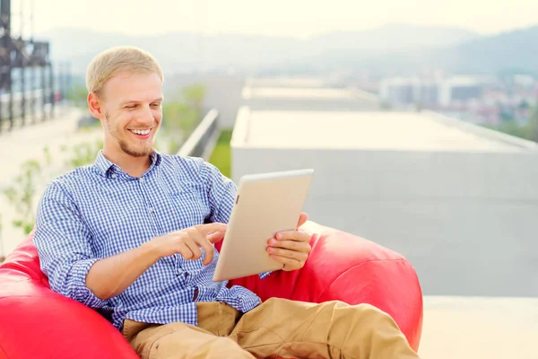Jovem Sorrindo Usando Computador Tablet Enquanto Sentado Saco Feijão Vermelho — Fotografia de Stock