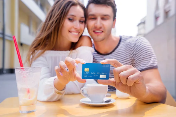 Attractive young couple holding plastic credit card while siting in sidewalk cafe.