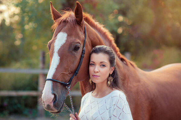 Portrait of young beautiful woman with brown horse at summer green park.