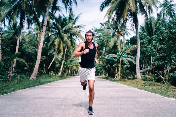 Young strong man is running under palm trees.