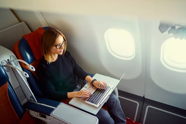 かなり若いビジネス女性飛行機に座りながらノート パソコンに取り組んで — ストック写真