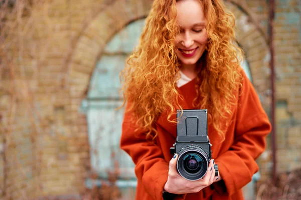 Long hair young woman with old fashioned camera taking pictures outdoors