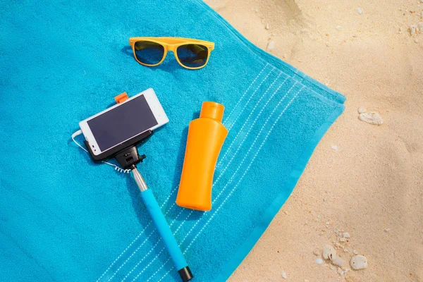 Vacation, technology and protection. Must have accessories on the sea beach. Smartphone, selfie stick, sunscreen and sunglasses