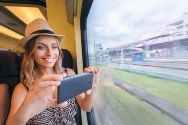 Genç smartphone, Window'u oturan trenle seyahat kadın fotoğrafı çekmek güzel.