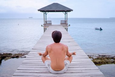 Lotus poz ahşap iskele üzerinde oturan genç adam. 