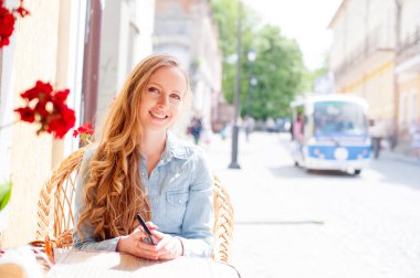 Kameraya bakarak kaldırımda kafede oturan genç çekici gülümseyen kadın.