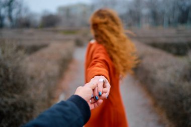 Arkadan görünüm açık havada erkek arkadaşının elini tutarak genç kadın uzun kızıl saç.