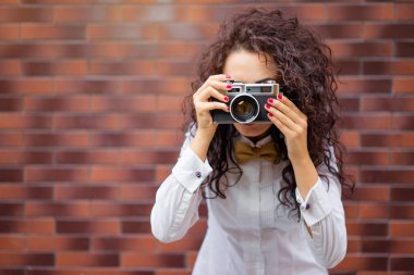 Duvara karşı dururken kamera tutan genç çekici esmer kadın.