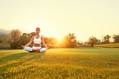 Lotus poz yeşil çimenlerin üzerinde oturan genç kadın. Sakin ve meditasyon kavramı.