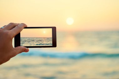  Erkek el smartphone, deniz günbatımı fotoğraf çekimi tutarak yakın çekim.