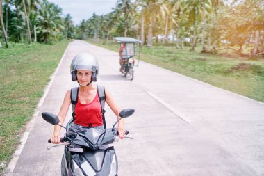 Kask binme scooter palmiye ağaçları ile yolda mutlu genç kadın.