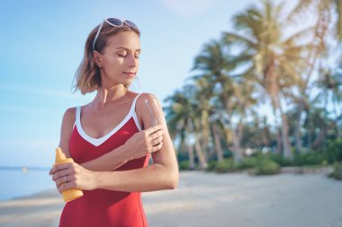 Tropikal kumsalda güneş losyonu ile şişe tutan genç güzel kadın.